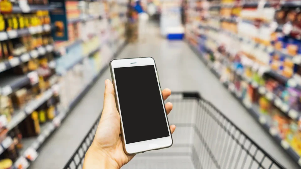 Hand Holding Smartphone with shopping cart in supermarket